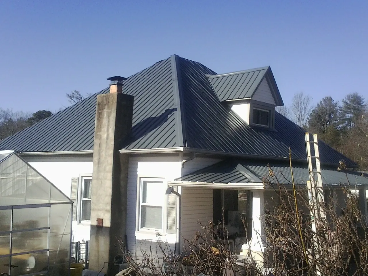 Dark blue standing seam metal roof on a white farmhouse with dormer in Virden