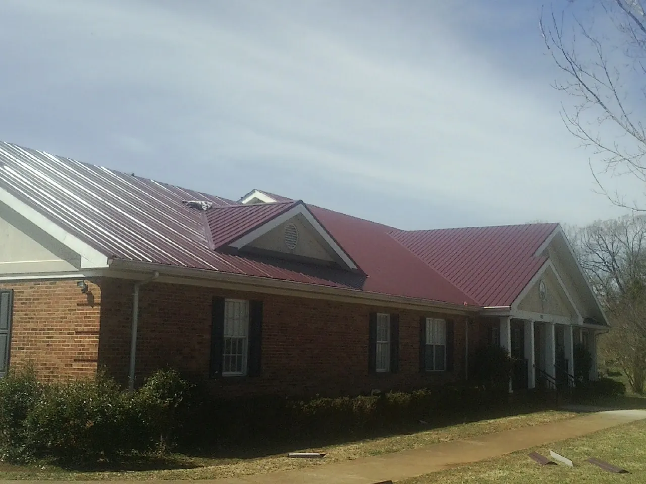 Red metal roof with gabled entries on a long brick building, from a Hail Damage Roof Repair job in Virden
