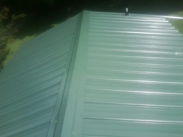 New green metal panels meeting at the ridge of a roof — Flat Roof Repair work by our crew in Virden