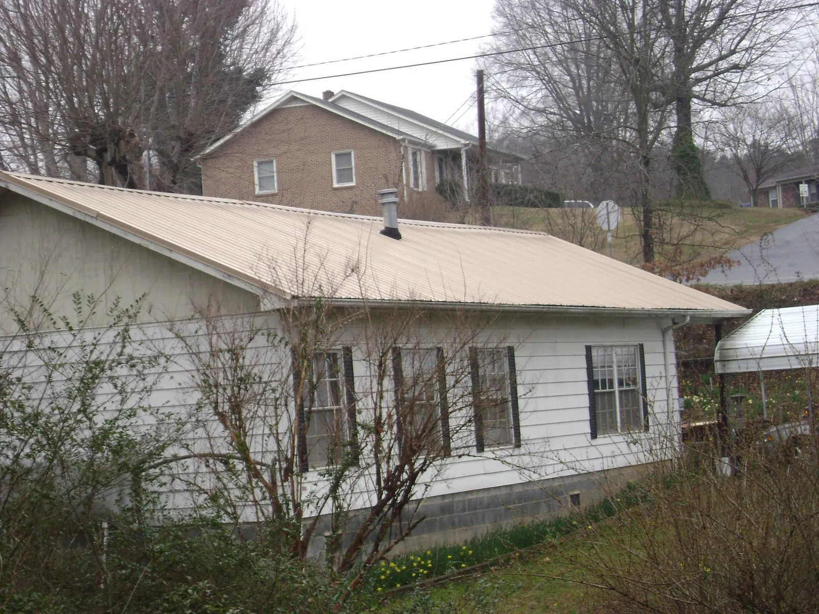 Tan metal roof on a white sided house set into a hillside — Commercial Roofing by Roofing Brothers in Virden